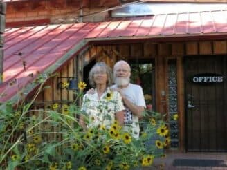 A man and woman stand together in front of an office building surrounded by sunflowers.