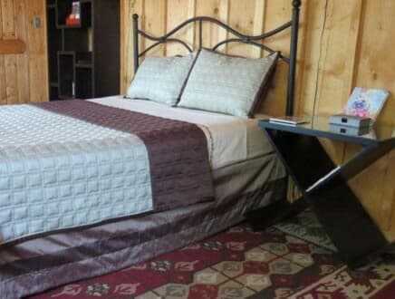 A neatly made bed with decorative pillows sits beside a modern side table on a patterned rug.
