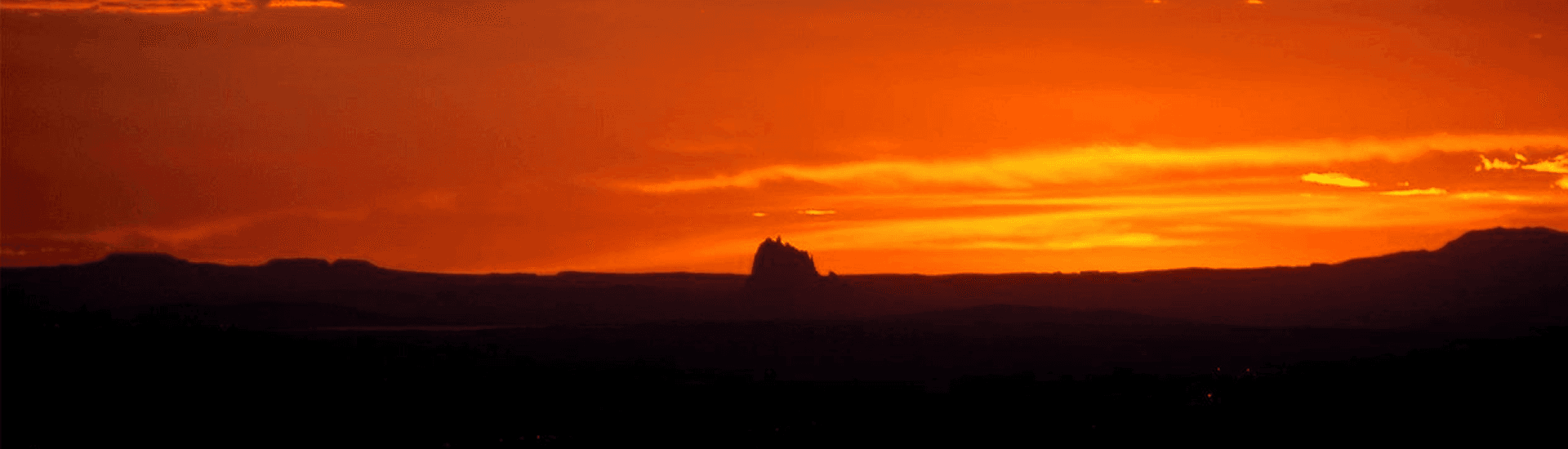 Silhouette of a mountain against a vibrant orange sunset.