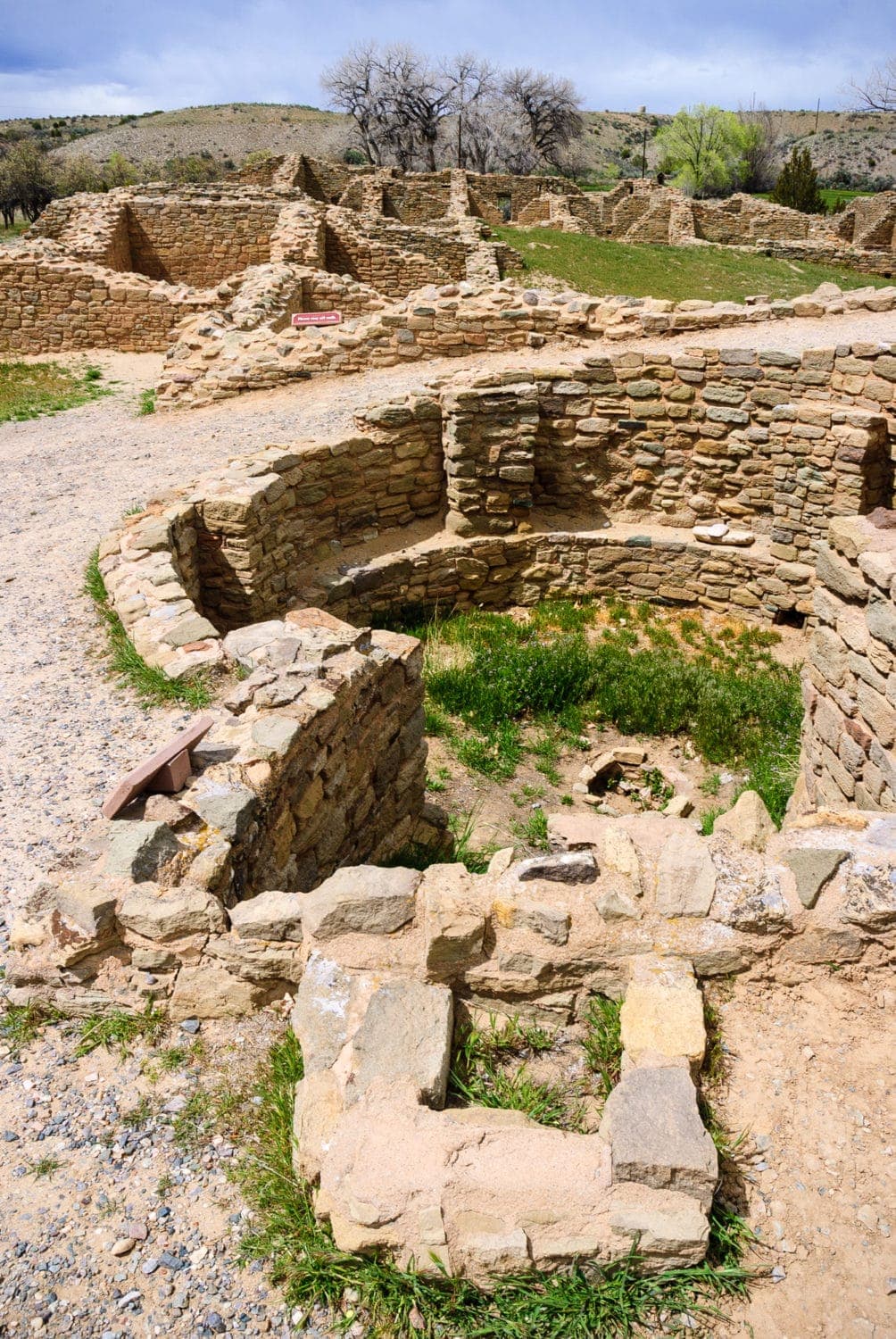 Remnants of ancient stone structures are surrounded by grassy areas under a cloudy sky.