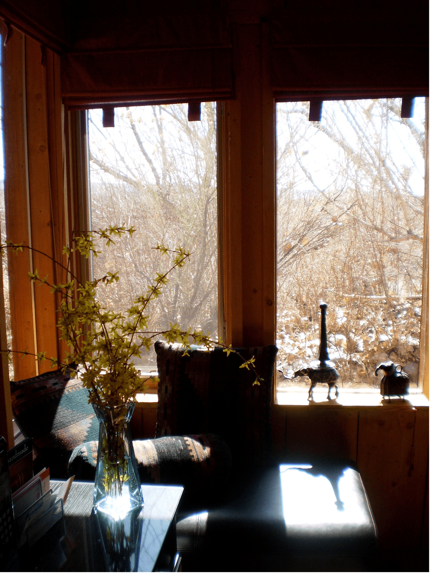 A cozy corner with a vase of flowers, a patterned chair, and sunlight streaming through windows.